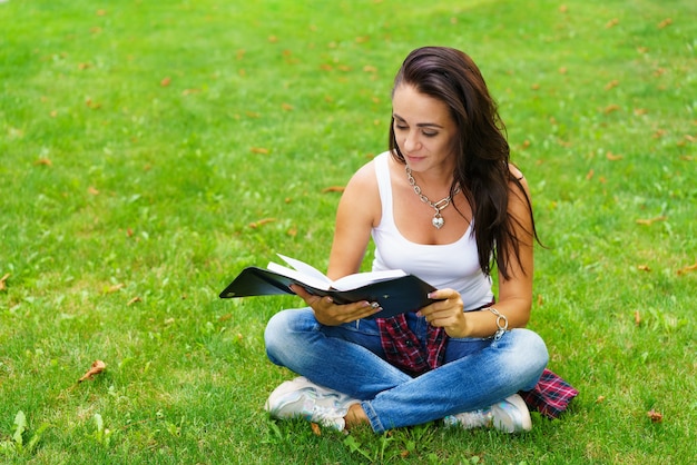 Mujer caucásica pensando y escribiendo notas en el cuaderno, chica atractiva planificando su trabajo, retrato de mujer sentada en el campo de hierba verde, concepto de ocio y relajación