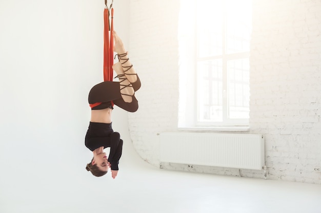 Mujer caucásica practicando asanas de yoga con mosca, colgando de la cabeza hacia abajo sobre fondo blanco en el gimnasio, copie el espacio. Salud, deporte, concepto de yoga