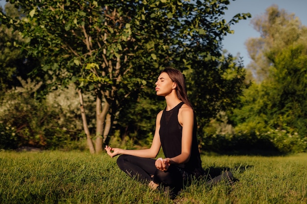 Mujer caucásica practicando meditación sentada en la hierba practicando yoga al atardecer