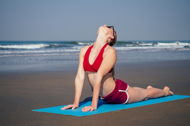 Mujer caucásica practicando yoga perro pose boca arriba en la orilla del mar