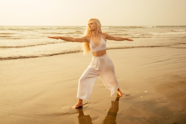 Mujer caucásica practicando yoga en pose de guerrero a orillas del mar