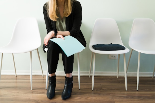 Mujer caucásica profesional sentada en la recepción y sosteniendo una carpeta con su currículum mientras espera una entrevista de trabajo. Mujer de negocios esperando una cita en una oficina de contratación