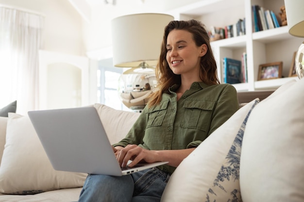 Una mujer caucásica que pasa tiempo en casa, sentada en el sofá, usando su computadora portátil. Estilo de vida en casa aislado, distanciamiento social en cuarentena durante la pandemia del coronavirus covid 19.