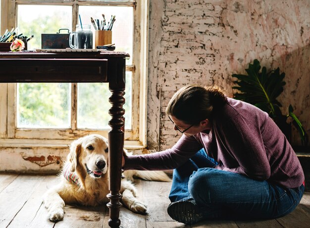 Mujer caucásica que se sienta en el piso de madera que acaricia el perro del golden retriever