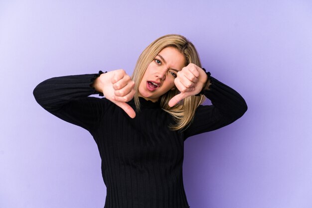 Mujer caucásica rubia joven aislada mostrando el pulgar hacia abajo y expresando aversión.