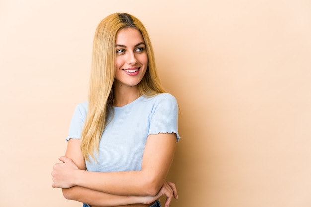 Mujer caucásica rubia joven que sonríe confiada con los brazos cruzados.