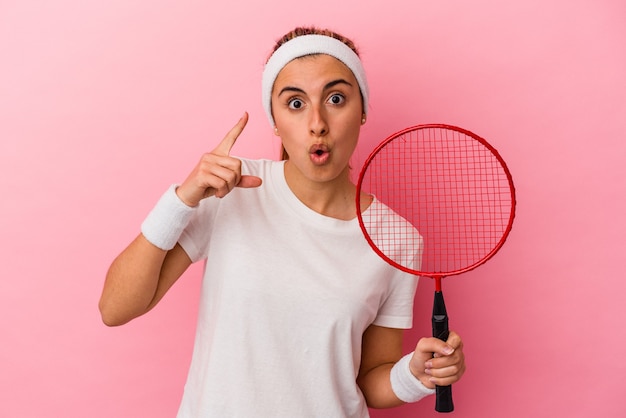 Mujer caucásica rubia linda joven que sostiene una raqueta de bádminton aislada en fondo rosado que tiene una idea, concepto de la inspiración.