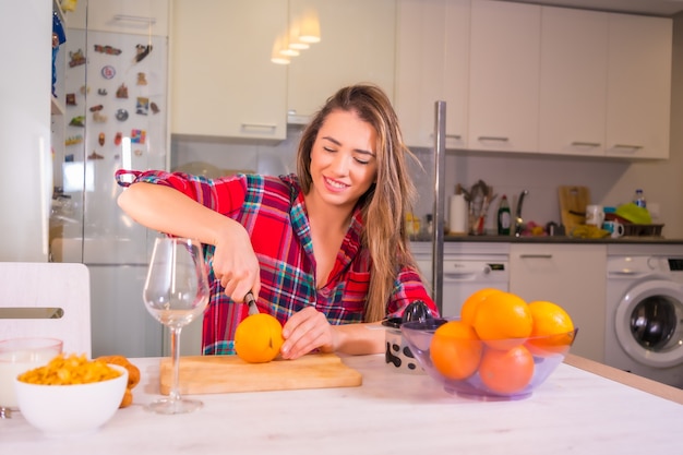 Mujer caucásica rubia con un zumo de naranja natural para el desayuno en su cocina