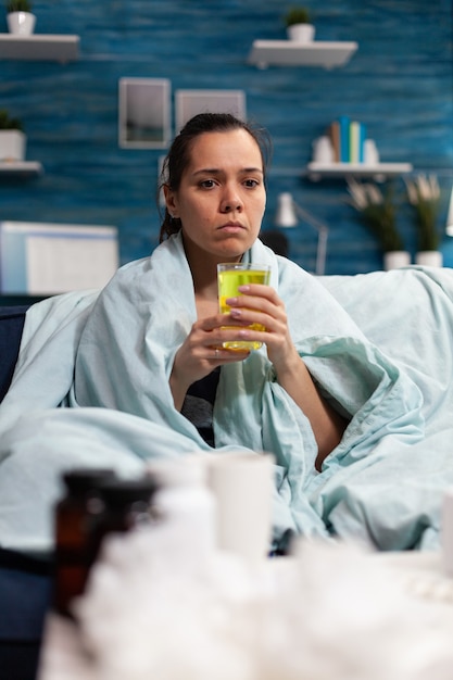 Mujer caucásica sentada en casa tomando medicamentos para la infección por virus mientras se siente enfermo adulto con fe ...