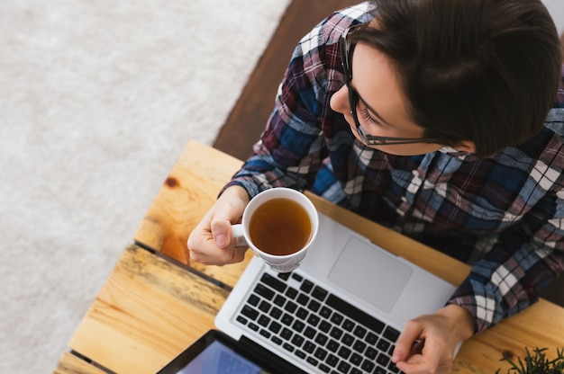 Mujer caucásica sentada frente a su laptop y sosteniendo una taza de té