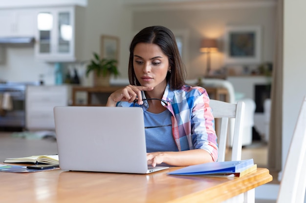 Mujer caucásica sentada junto al escritorio trabajando desde casa usando una computadora portátil