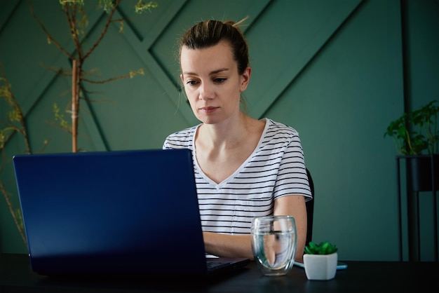 Mujer caucásica sentada a la mesa en la oficina de su casa y trabaja con una laptop independiente que trabaja de forma remota