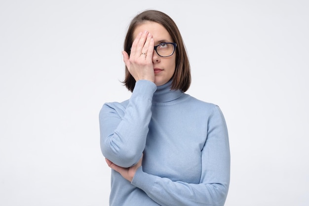 Una mujer caucásica seria con gafas se cubrió la cara con la mitad de la mano