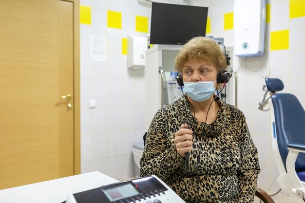 Una mujer caucásica se sienta con auriculares para comprobar su audición en el consultorio de un audiólogo