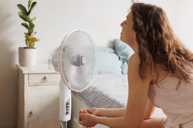 Foto la mujer caucásica se sienta frente a un ventilador de aire acondicionado y se enfría en el calor del verano
