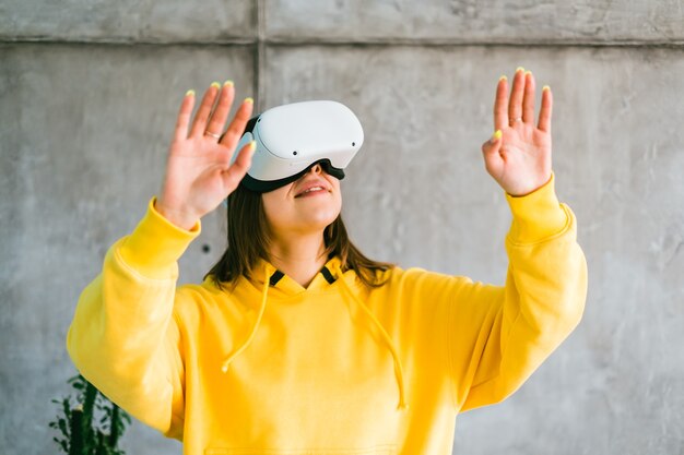 Mujer caucásica sonriente joven que usa el casco de Vr, gesticulando y mirando hacia arriba en la realidad virtual.