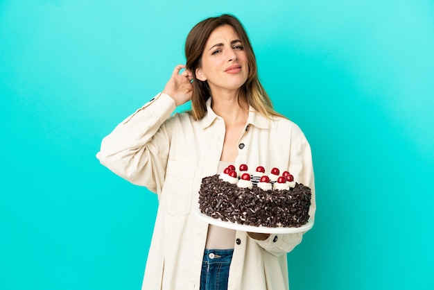 Mujer caucásica sosteniendo pastel de cumpleaños aislado sobre fondo azul con dudas