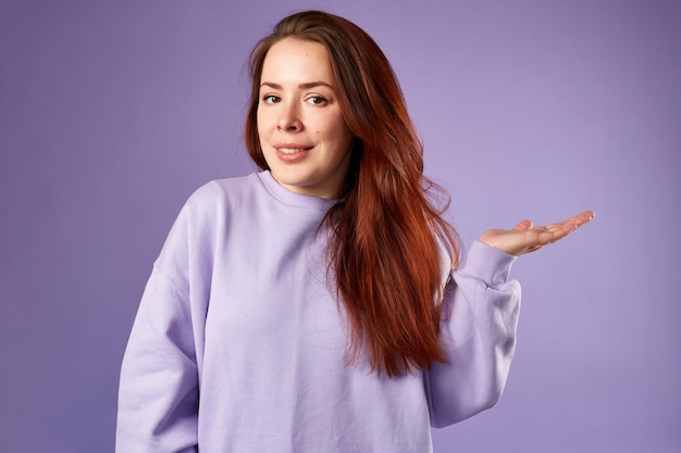 Mujer caucásica en sudadera violeta Aspecto natural Cabello largo y rojo sonriente Fondo violeta