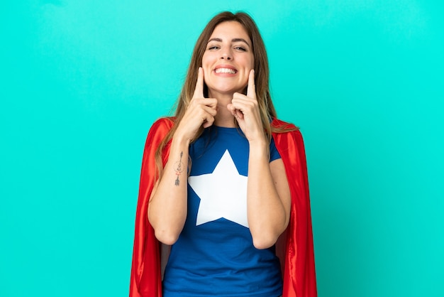 Mujer caucásica de superhéroe aislada en la pared azul sonriendo con una expresión feliz y agradable