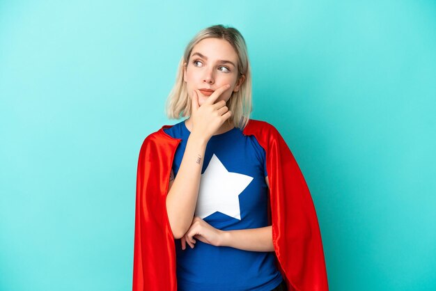 Mujer caucásica de superhéroe aislada sobre fondo azul que tiene dudas y con expresión de la cara confusa