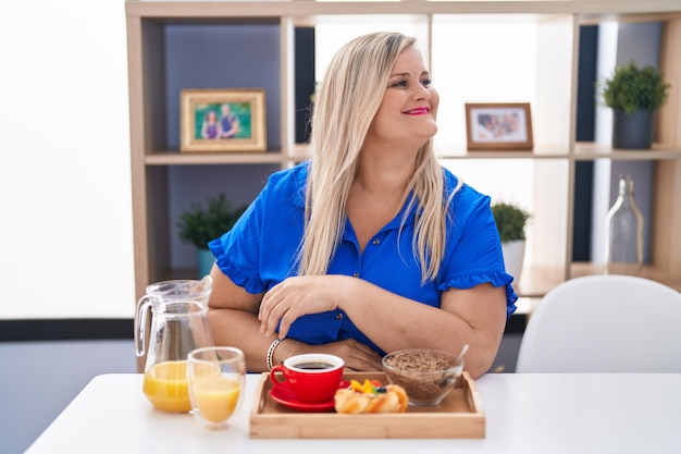 Mujer caucásica de talla grande desayunando en casa mirando de lado a lado con una sonrisa en la cara, expresión natural. riendo confiado.