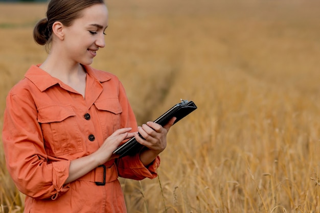 Mujer caucásica tecnólogo agrónomo con tablet PC en el campo de trigo, control de calidad y crecimiento de cultivos para la agricultura. Concepto de agricultura y cosecha.