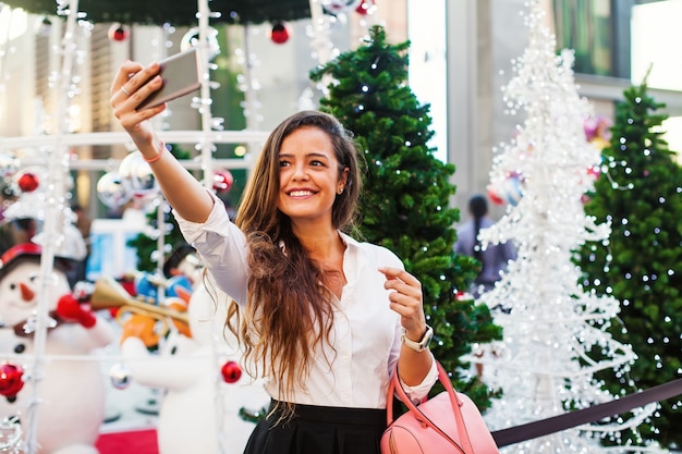 Mujer caucásica tomando selfie delante del árbol de Navidad