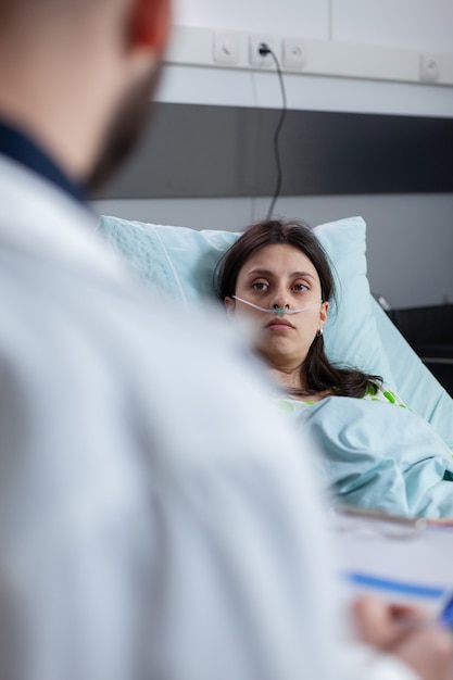 Mujer caucásica con tubo de oxígeno nasal descansando en la cama en la sala del hospital
