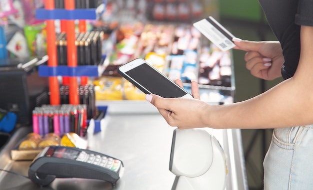 Mujer caucásica usando teléfono inteligente y con tarjeta de crédito en el supermercado