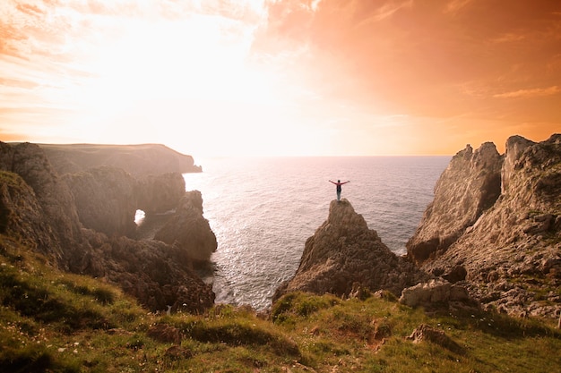 Mujer celebrando una puesta de sol en la cima de una montaña con vistas al océano