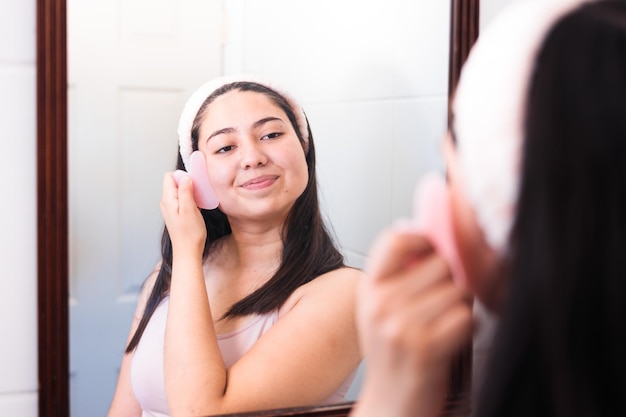 Una mujer se cepilla la cara frente a un espejo y mira su lápiz labial rosa.