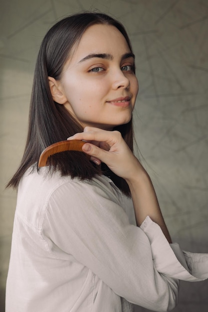 mujer cepillando el cabello lacio con peine de madera natural y haciendo rutina de cuidado del cabello