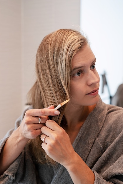 Mujer cepillándose el pelo y sonriendo mientras mira en el espejo