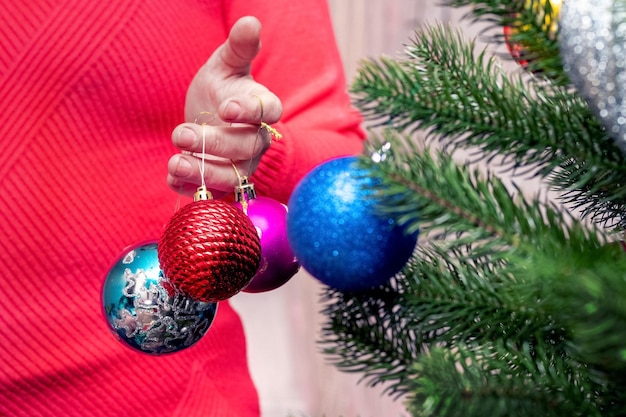 Una mujer cerca del árbol de Navidad tiene adornos navideños en la mano.