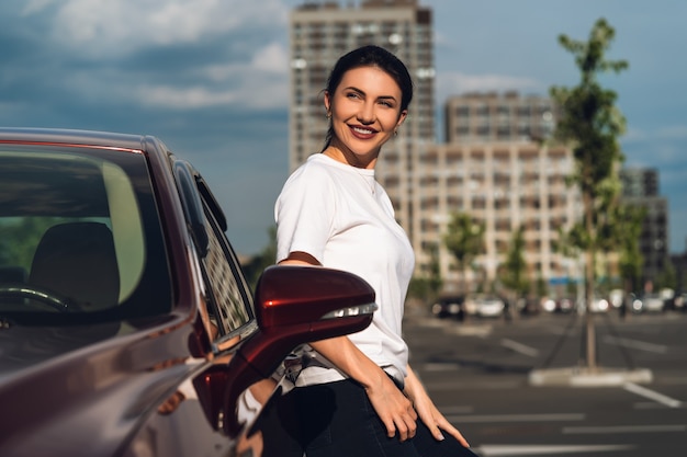 La mujer se para cerca del auto nuevo en el estacionamiento.