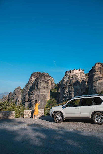 Mujer cerca de un auto suv tomando una foto del monasterio de meteora en las montañas de tesalia