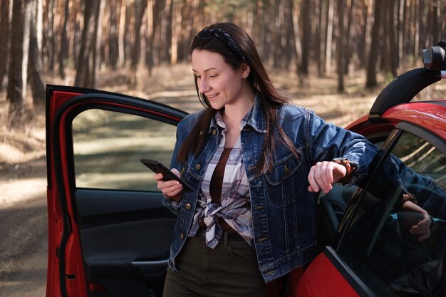 Una mujer se para cerca de un automóvil mirando a un teléfono inteligente.