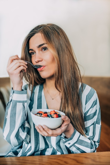 Mujer de cerca comiendo avena y tazón de frutas para el desayuno