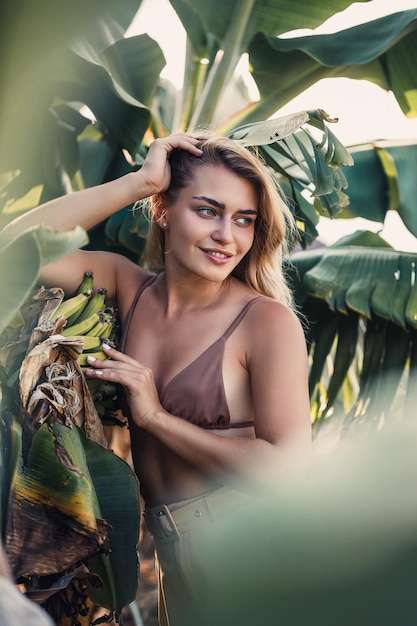 Una mujer se para cerca de hojas de plátano verde en la isla Árboles tropicales