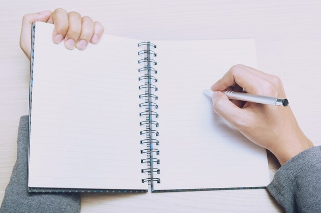 Mujer de cerca la mano está escribiendo el costo del bloc de notas en el libro sentarse en el sofá.