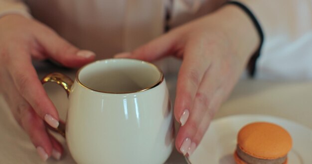 Mujer de cerca en pijama de pie en la cocina soleada por la mañana bebiendo café o té caliente