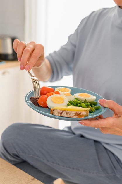 Mujer de cerca sostiene un desayuno saludable de huevos duros y verduras al vapor en un plato equilibrado