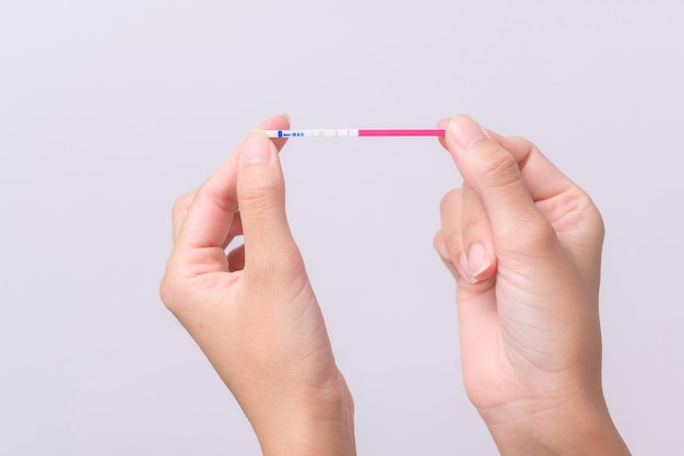 Mujer de cerca usando la prueba de ovulación LH o la prueba de embarazo HCG sobre fondo blanco