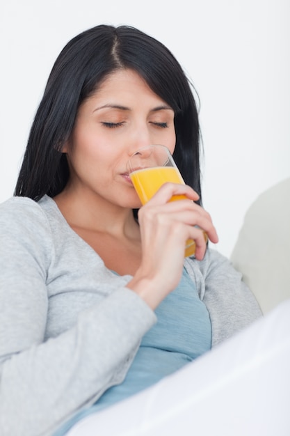 Mujer cerrando los ojos mientras bebe de un vaso de jugo de naranja