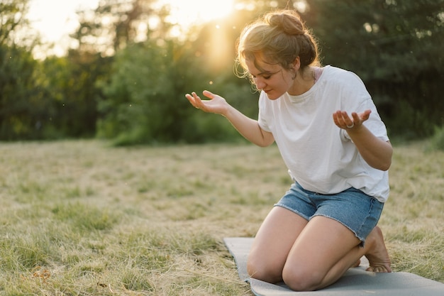 La mujer cerró los ojos rezando en un campo durante la hermosa puesta de sol manos dobladas en concepto de oración por ...