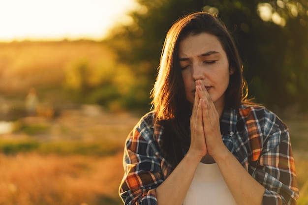 La mujer cerró los ojos rezando en un campo durante la hermosa puesta de sol