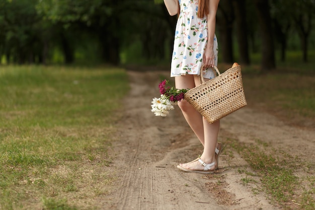 Mujer con una cesta de mimbre y flores en un camino rural.