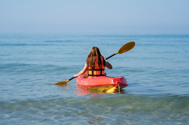 mujer en chaleco salvavidas remando un kayak en el mar