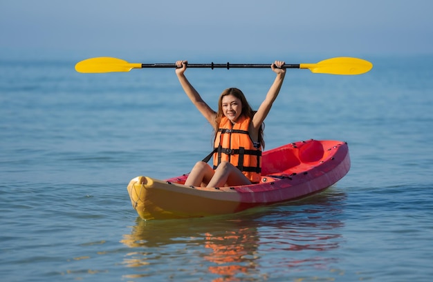 Mujer con chaleco salvavidas remando en un kayak en el mar