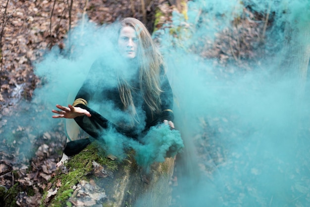 Mujer chamán con la mano una bomba de humo verde en el tronco de un árbol en un día de primavera